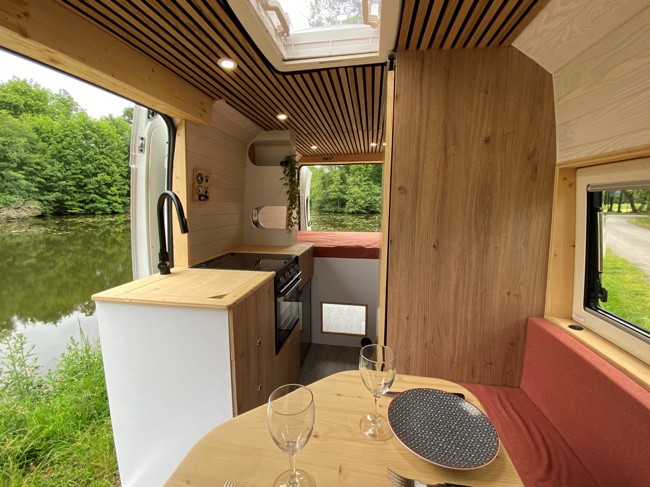 Aménagement intérieur d'un van en Bretagne réalisé par un aménageur professionnel. Le van comprend des meubles en bois sur mesure, une kitchenette entièrement équipée, et un coin salon convertible en lit. L'espace est optimisé pour maximiser le confort et la fonctionnalité. Stationné près d'une plage bretonne, ce van aménagé illustre la qualité et l'attention aux détails du travail de l'aménageur, parfait pour explorer les paysages bretons.