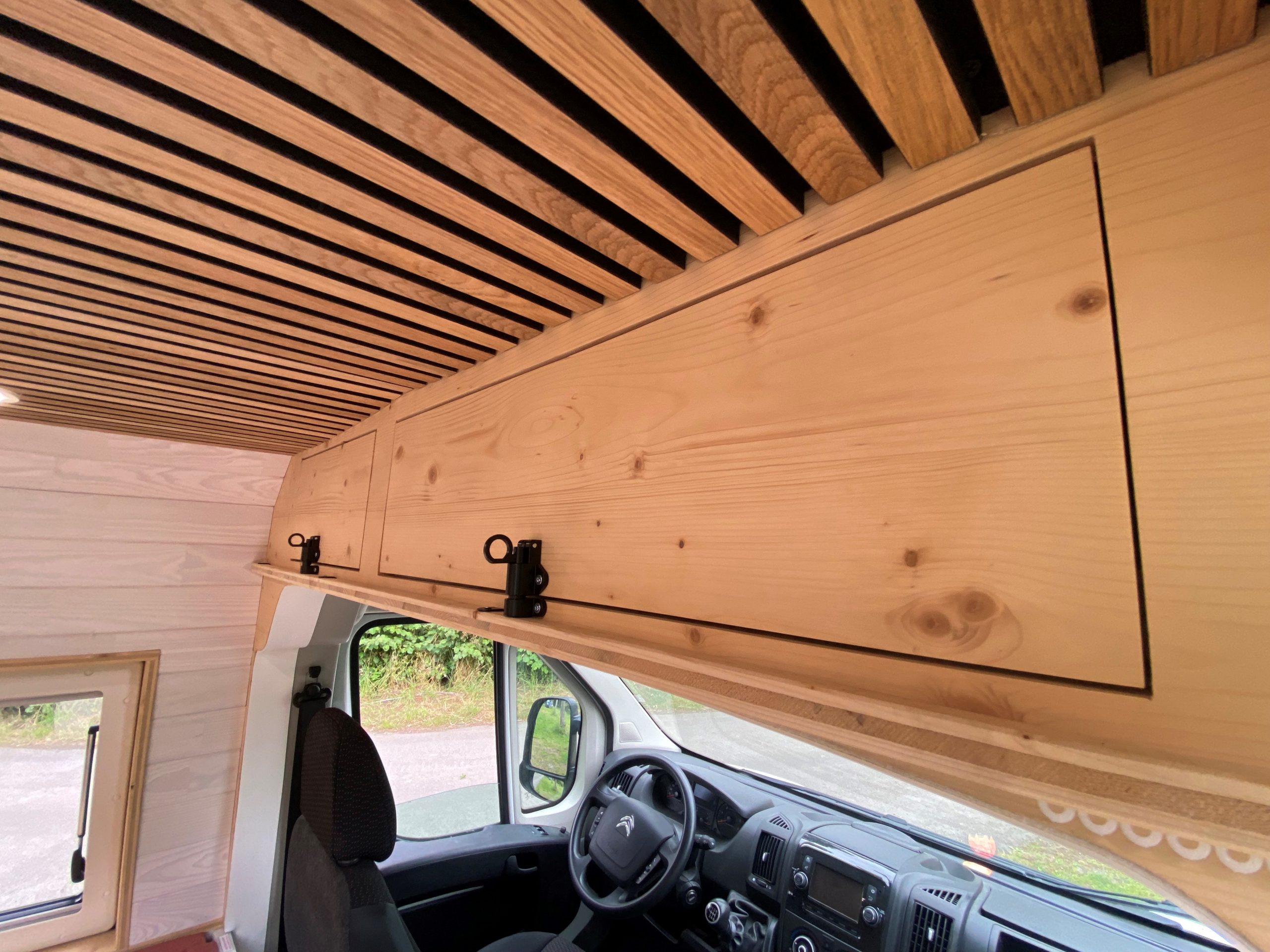 Aménagement de van en Bretagne par un expert. Intérieur élégant avec meubles en bois sur mesure, kitchenette équipée, et salon convertible en lit confortable. Ce van aménagé offre un espace optimisé et fonctionnel, idéal pour les road trips à travers la Bretagne. Exemple parfait de l'aménagement de van haut de gamme.