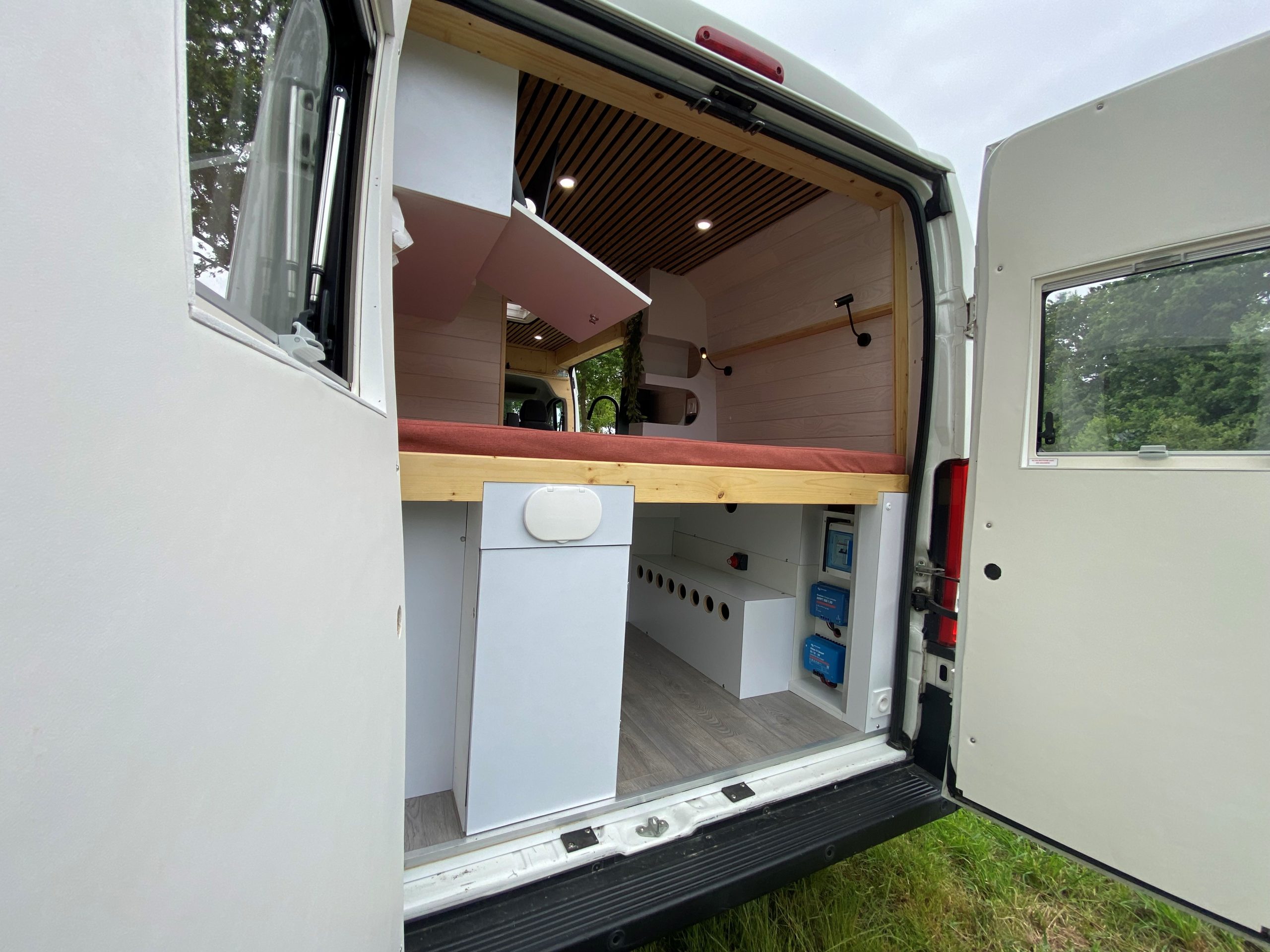 Intérieur de van aménagé en Bretagne par un professionnel. Design astucieux avec kitchenette, coin salon et lit intégré. Idéal pour les road trips et l'exploration des paysages bretons. Exemple d'un aménagement de van réussi, alliant confort et praticité.